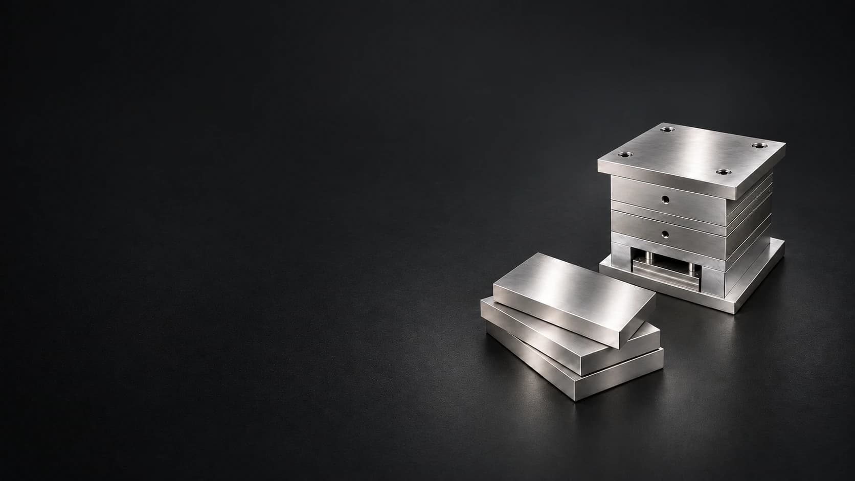 Clearly lit finished steel plates and an assembled mold base on a matte charcoal floor
